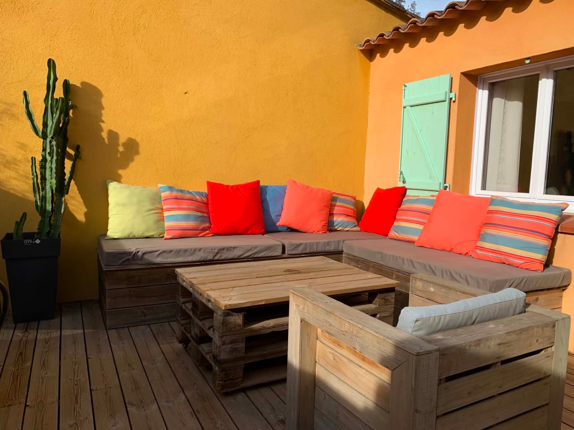 Coin salon extérieur de la Villa Dypsis avec banquette en palettes et coussins colorés
